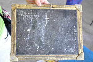 Tribal kids practise writing using chalks and chalkboards made of black cardboard.